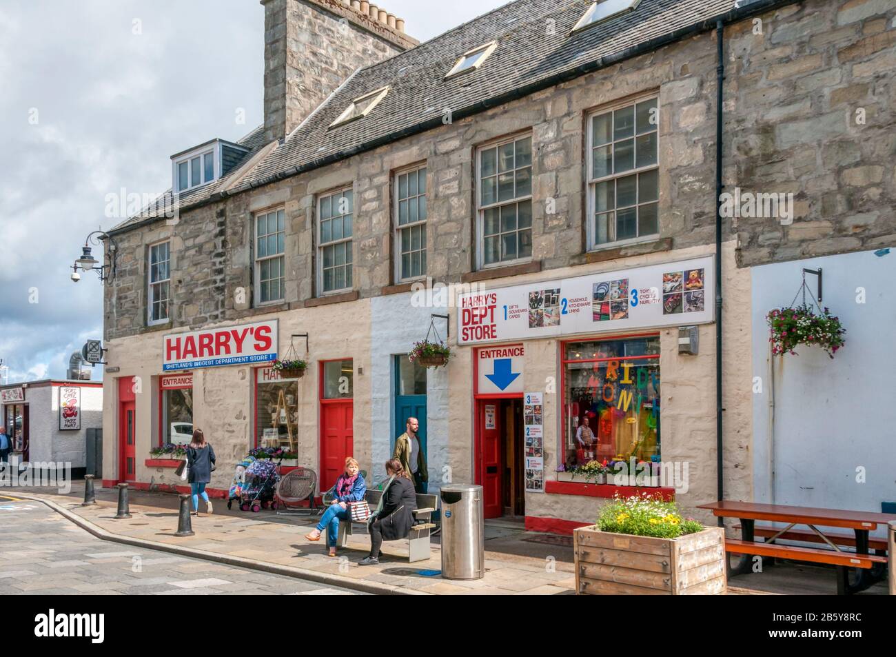 Les gens assis au soleil à l'extérieur de Harry's, le plus grand grand magasin de Shetland à Lerwick. Banque D'Images