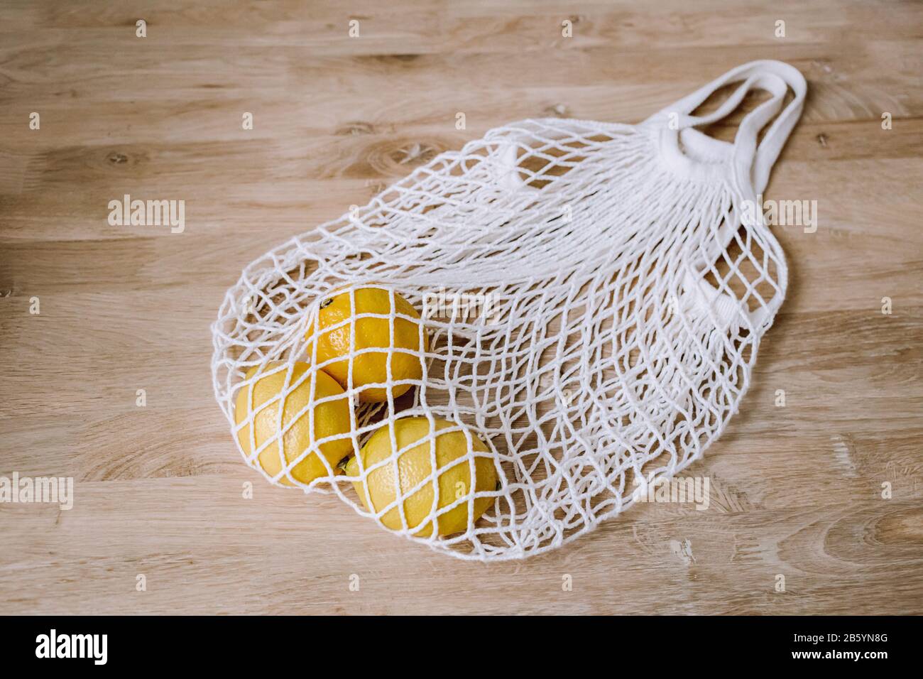 Sac à cordes blanc avec citrons jaunes sur fond en bois. Produits écologiques à usage général. Écologique, sans plastique. Vue de dessus. Banque D'Images