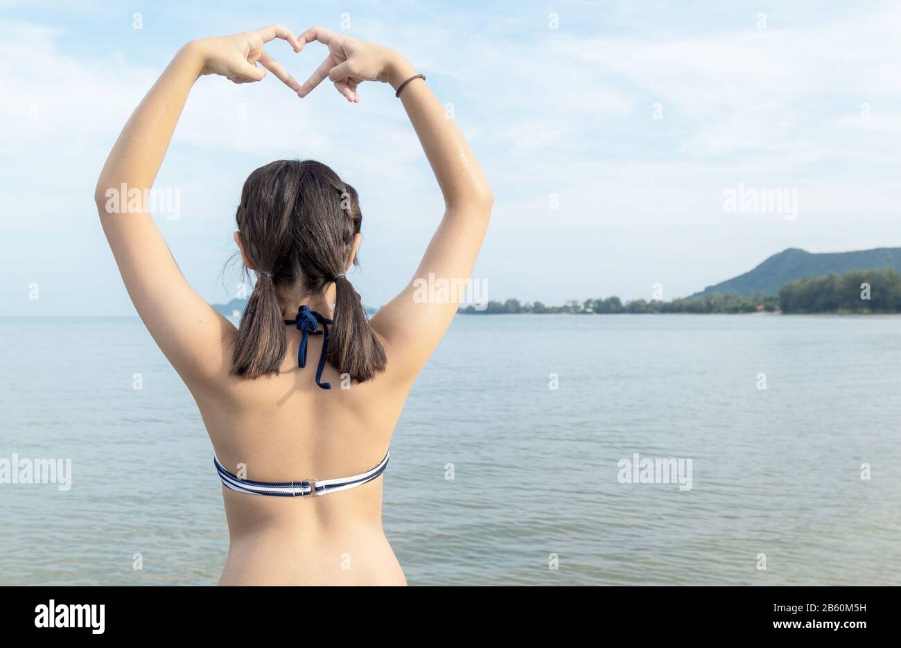 Les adolescentes asiatiques portant le bikini et la main gestuelle langue se traduit par l'amour à la plage avec l'espace de copie. Banque D'Images
