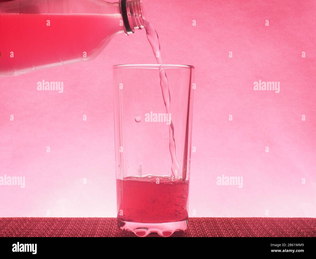 Une boisson gazeuse rose est versée dans un verre transparent. Photo sur un fond rose. Toujours la vie Banque D'Images