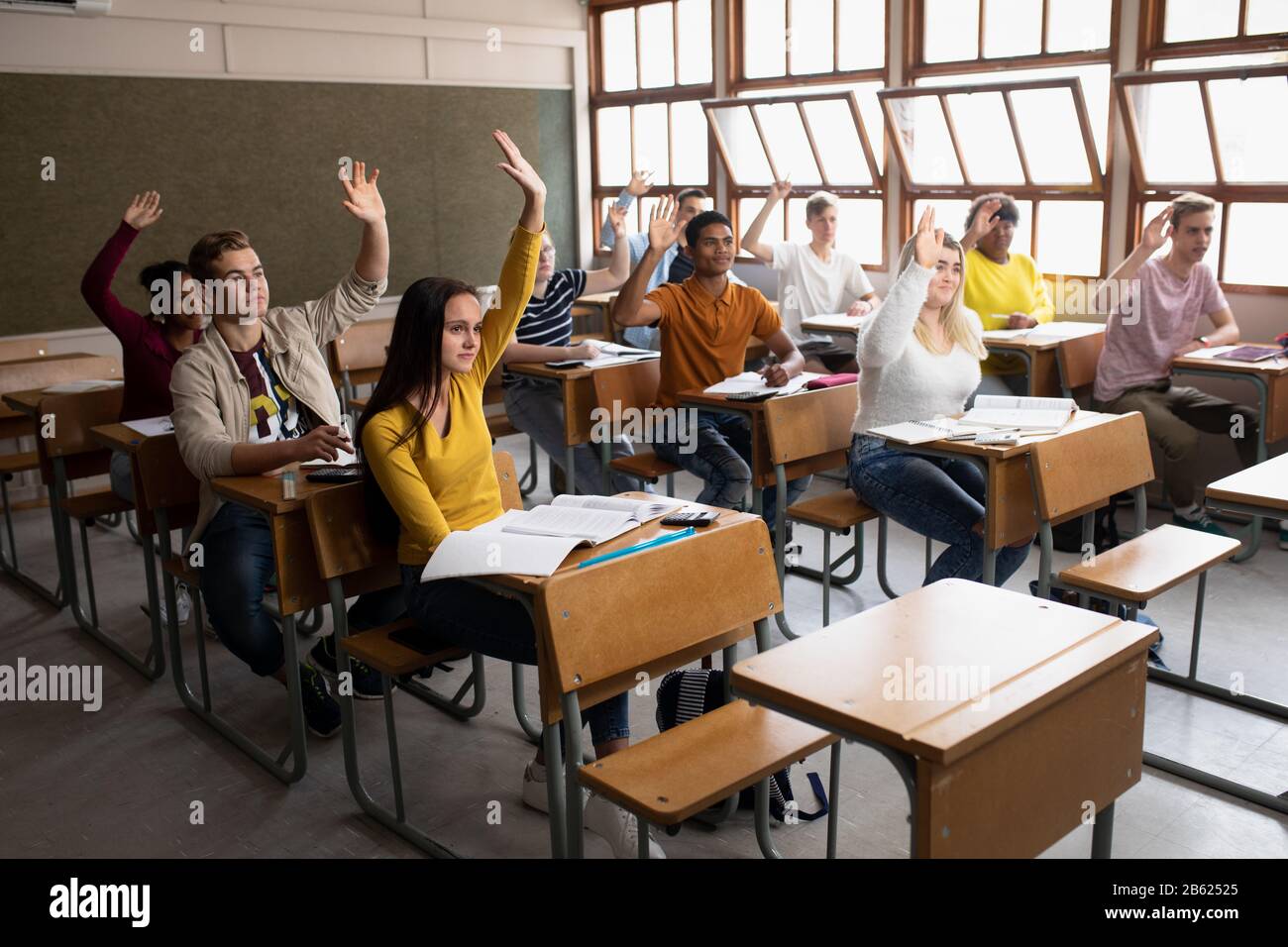 Vue latérale des élèves levant les mains en classe Banque D'Images