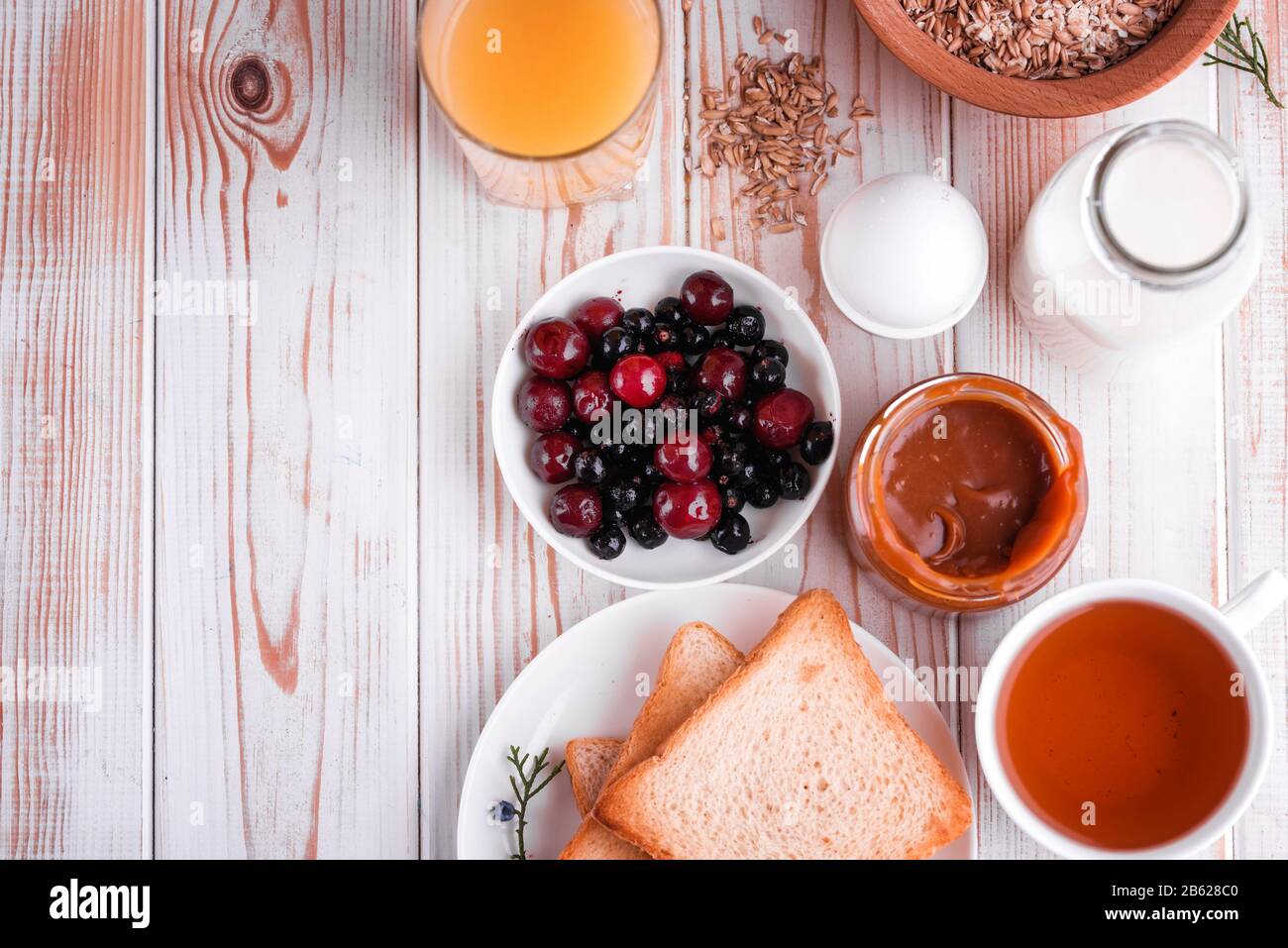 Délicieux petit déjeuner sain et copieux sur la table blanche. Œufs, flocons d'avoine, lait, thé, pain grillé à la banane, caramel salé maison, crêpes aux fruits, orange Banque D'Images