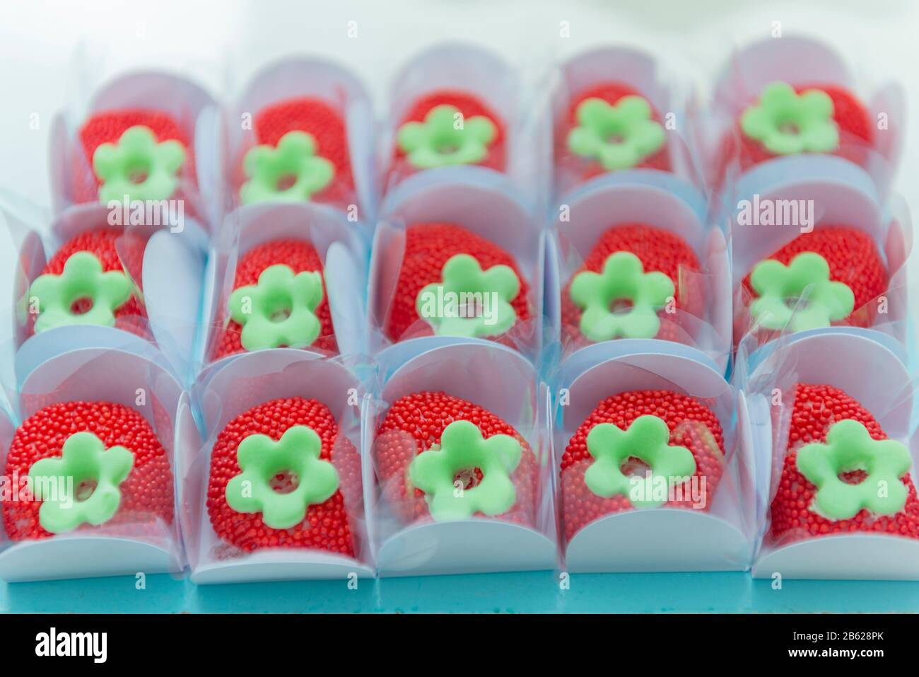 Bonbons de fête pour enfants en forme de fraise. Bonbons saupoudrés rouges dans une boîte en papier blanc sur un plateau bleu avec peu de profondeur de champ. Mise au point sélective. Banque D'Images