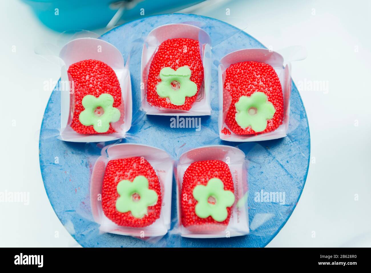 Bonbons de fête pour enfants en forme de fraise. Bonbons saupoudrés rouges dans une boîte en papier blanc sur un plateau bleu avec peu de profondeur de champ. Mise au point sélective. Banque D'Images