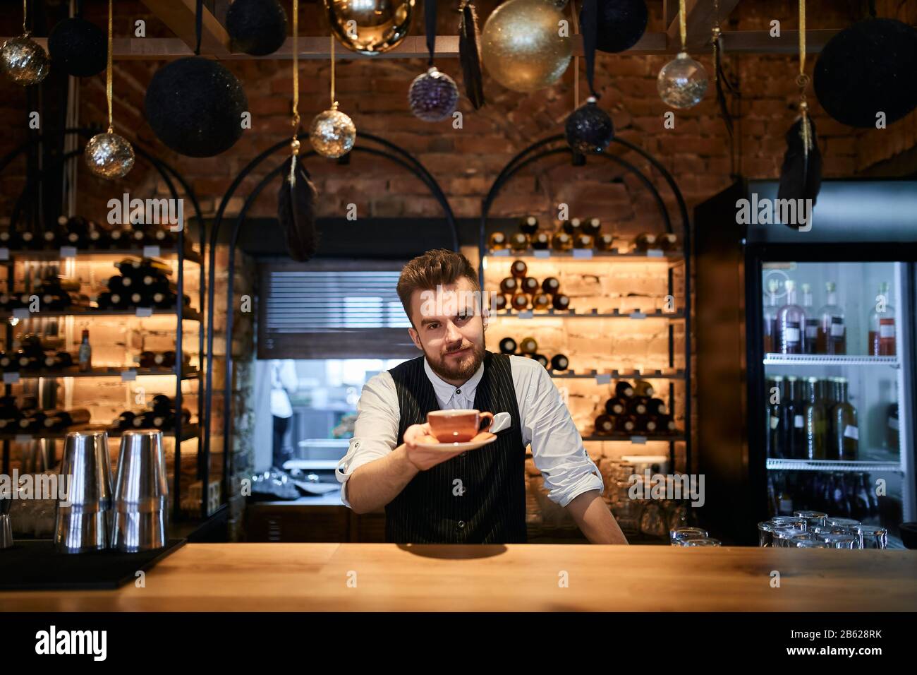 Gros plan sur le Barista barbu portant une tasse de café dans la main regardant la caméra au café, gros plan photo.job, profession, profession Banque D'Images
