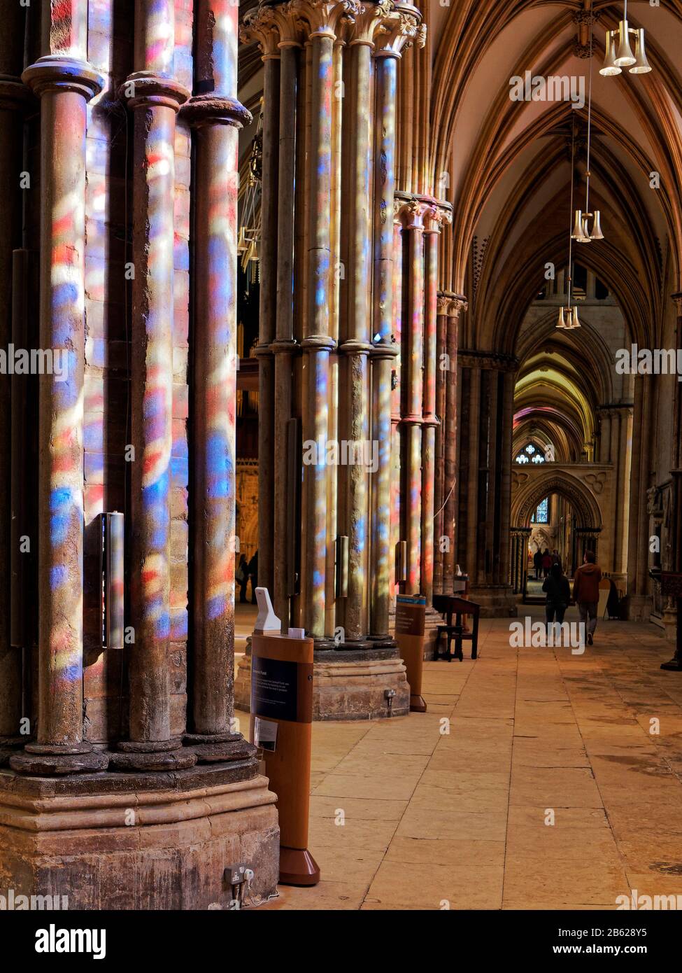 Les vitraux de la cathédrale de Lincoln ont jeté des couleurs tachetées sur les colonnes de la nef lors d'une journée de printemps. Banque D'Images