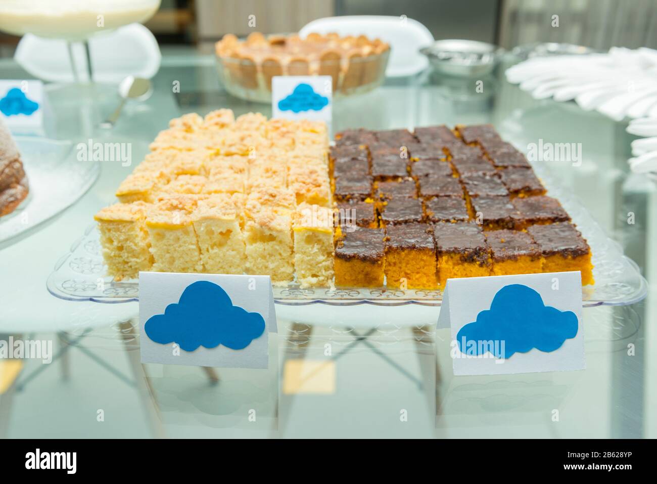 Plateau avec deux types de gâteaux faits à la main. Gâteau aux carottes recouvert de chocolat et gâteau aux semoules de maïs sur table en verre. Gâteaux coupés en morceaux carrés. Banque D'Images