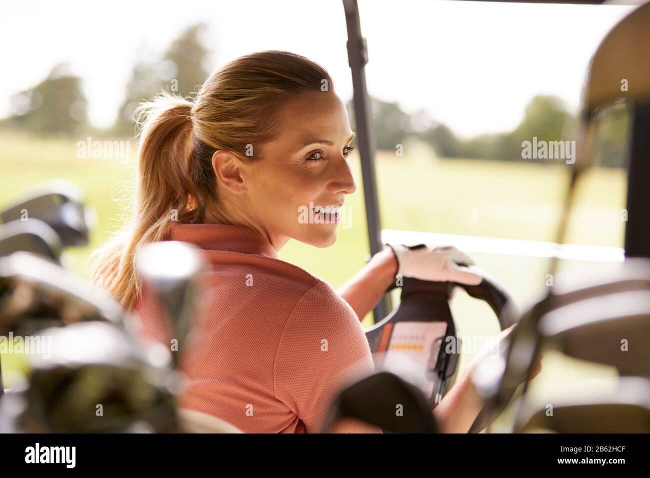 Vue Arrière De La Femme Mûre Jouant Au Golf Conduite Buggy Le Long Du Parcours Vue Par Les Clubs De Golf Banque D'Images