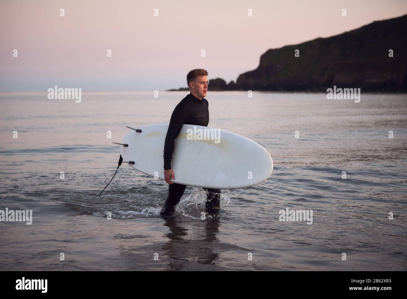 Homme Portant Des Wetsuit Transportant Surfboard LorsQu'Il Sort De La Mer Banque D'Images