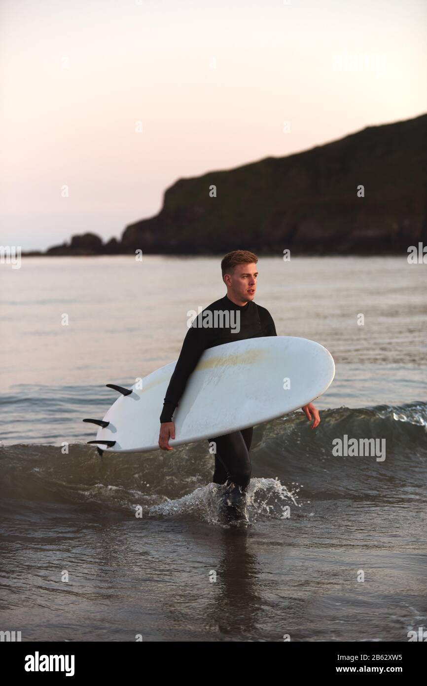 Homme Portant Des Wetsuit Transportant Surfboard LorsQu'Il Sort De La Mer Banque D'Images