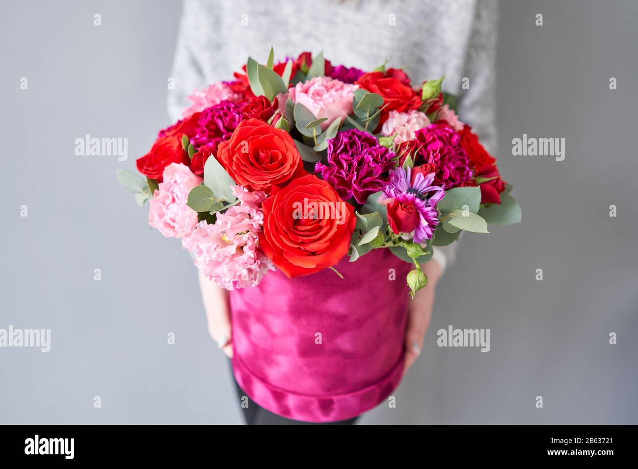 Bouquet de fleurs rouges et violettes dans une boîte ronde en velours. Boutique européenne de fleurs. Bouquet de belles fleurs mixtes dans la main de la femme. Banque D'Images