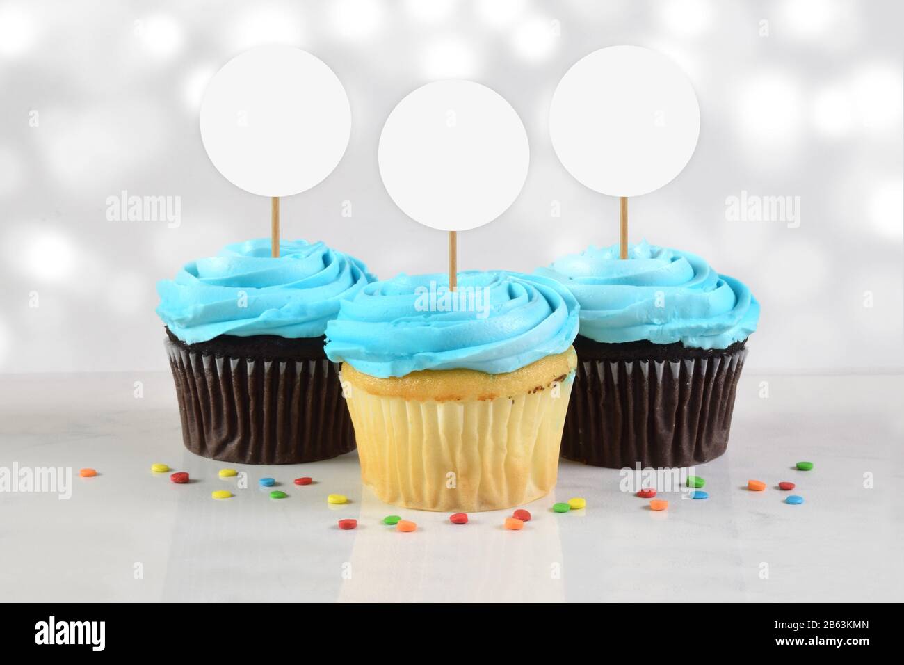 Cette maquette de cupcake comprend trois délicieux cupcakes bleus dépoli au sommet d'un fond en marbre blanc dépoli aux chevilles colorées. Le brillant W Banque D'Images