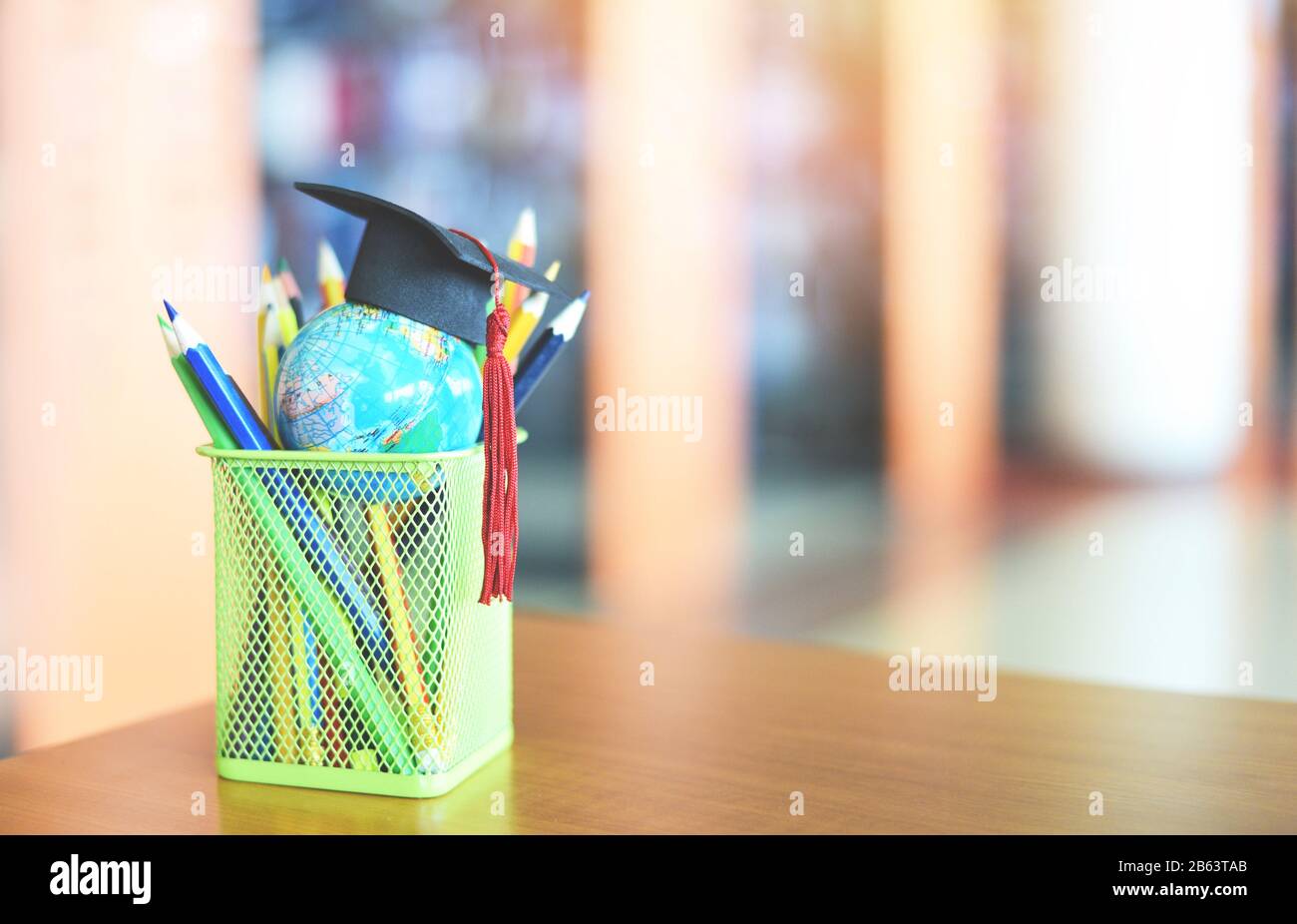 Éducation apprentissage et retour à l'école avec un chapeau de graduation sur un étui crayon sur la table dans la bibliothèque contexte / chapeau de graduation sur terre globe mode Banque D'Images