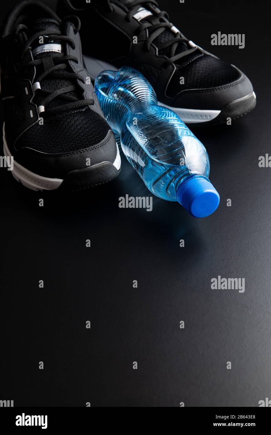 Concept de forme physique. Chaussures de sport noires et bouteille d'eau sur fond noir. Banque D'Images