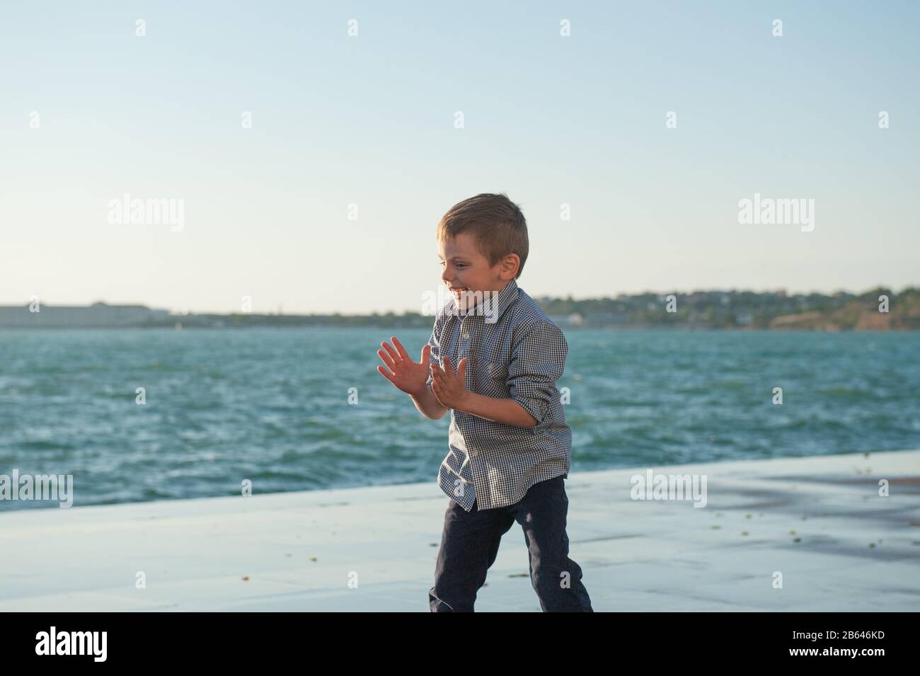 drôle heureux actif petit enfant applaudit avec joie jouer sur la côte de la mer dans la ville portuaire par temps de tempête de printemps Banque D'Images