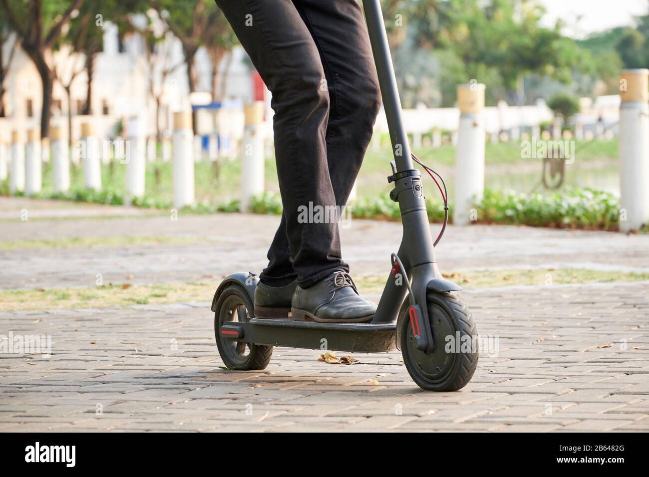 Image courte de jeune homme d'affaires qui monte sur un scooter électrique de kick dans le parc de la ville et qui se fait mal au travail Banque D'Images