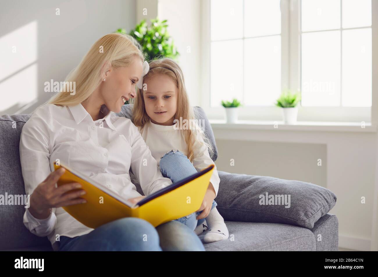 La mère et la fille lisent un livre tout en s'asseyant sur un canapé dans une chambre avec une fenêtre. Banque D'Images