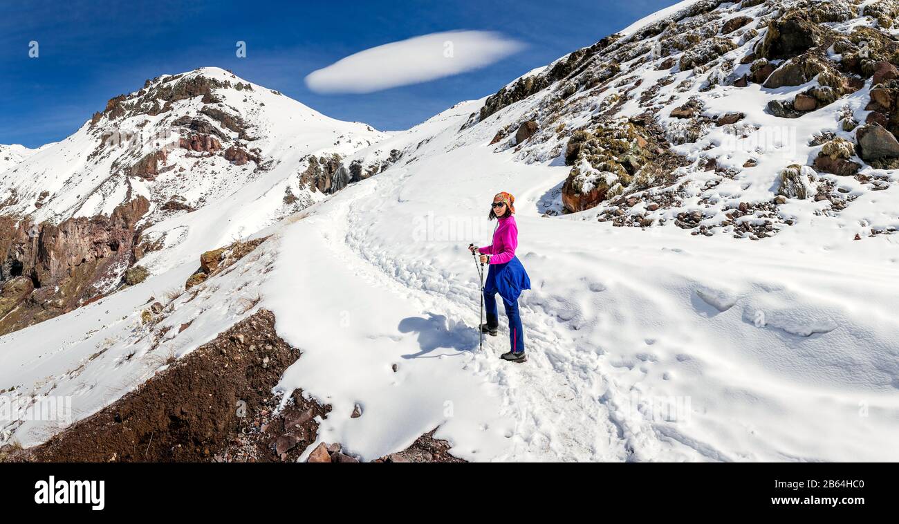 Femme randonnée sur un sentier enneigé dans les montagnes du Caucase sur le fond d'un nuage lenticulaire inhabituel Banque D'Images