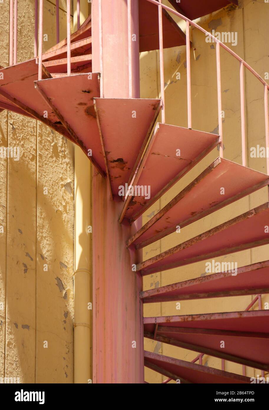 Escalier en colimaçon allant du sol au sol à l'extérieur d'un bâtiment peint de couleur jaune. Banque D'Images