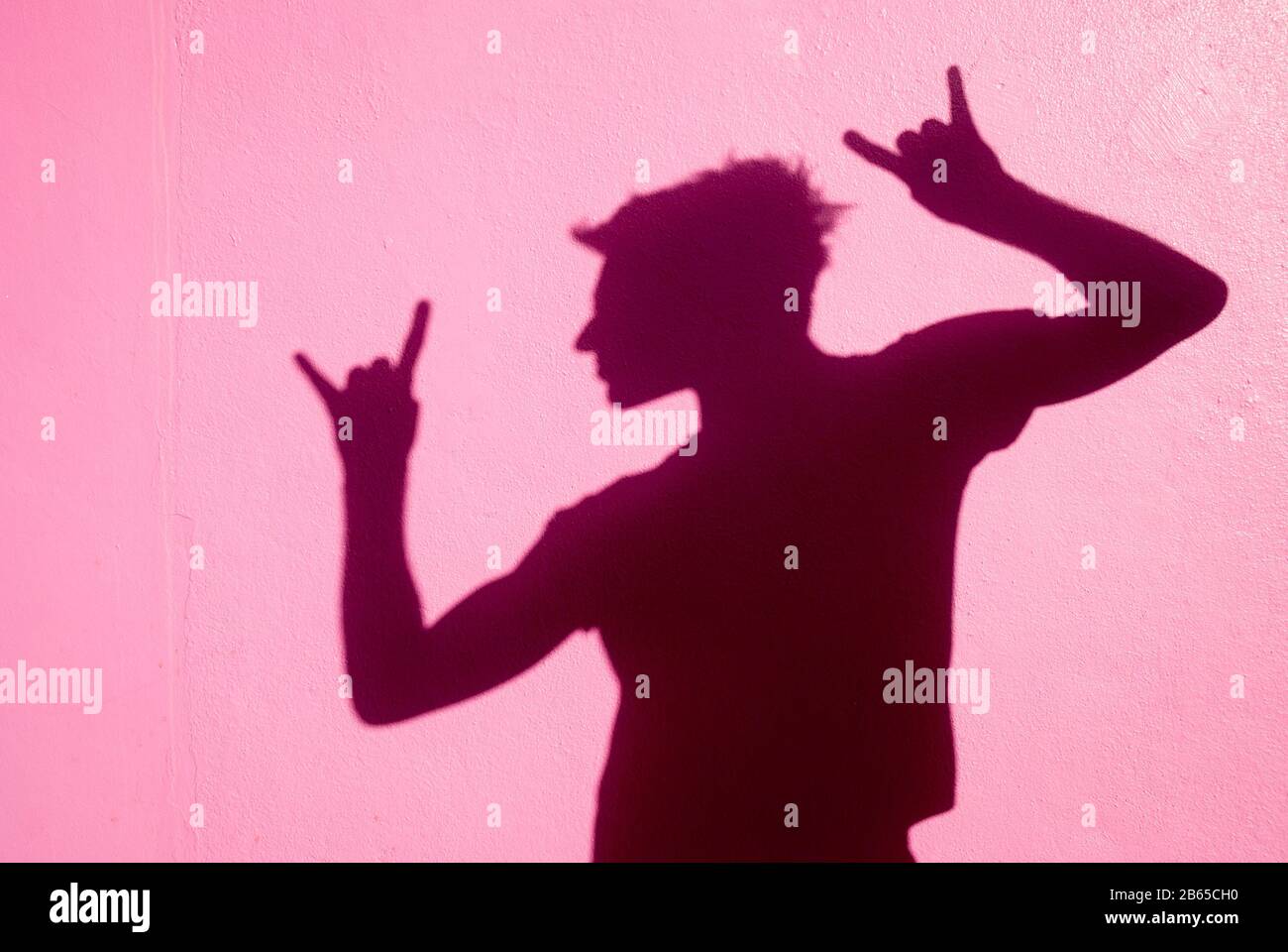 L'ombre d'un homme méconnaissable qui met le rock n rouler les mains à  l'extérieur contre un mur rose vif Photo Stock - Alamy