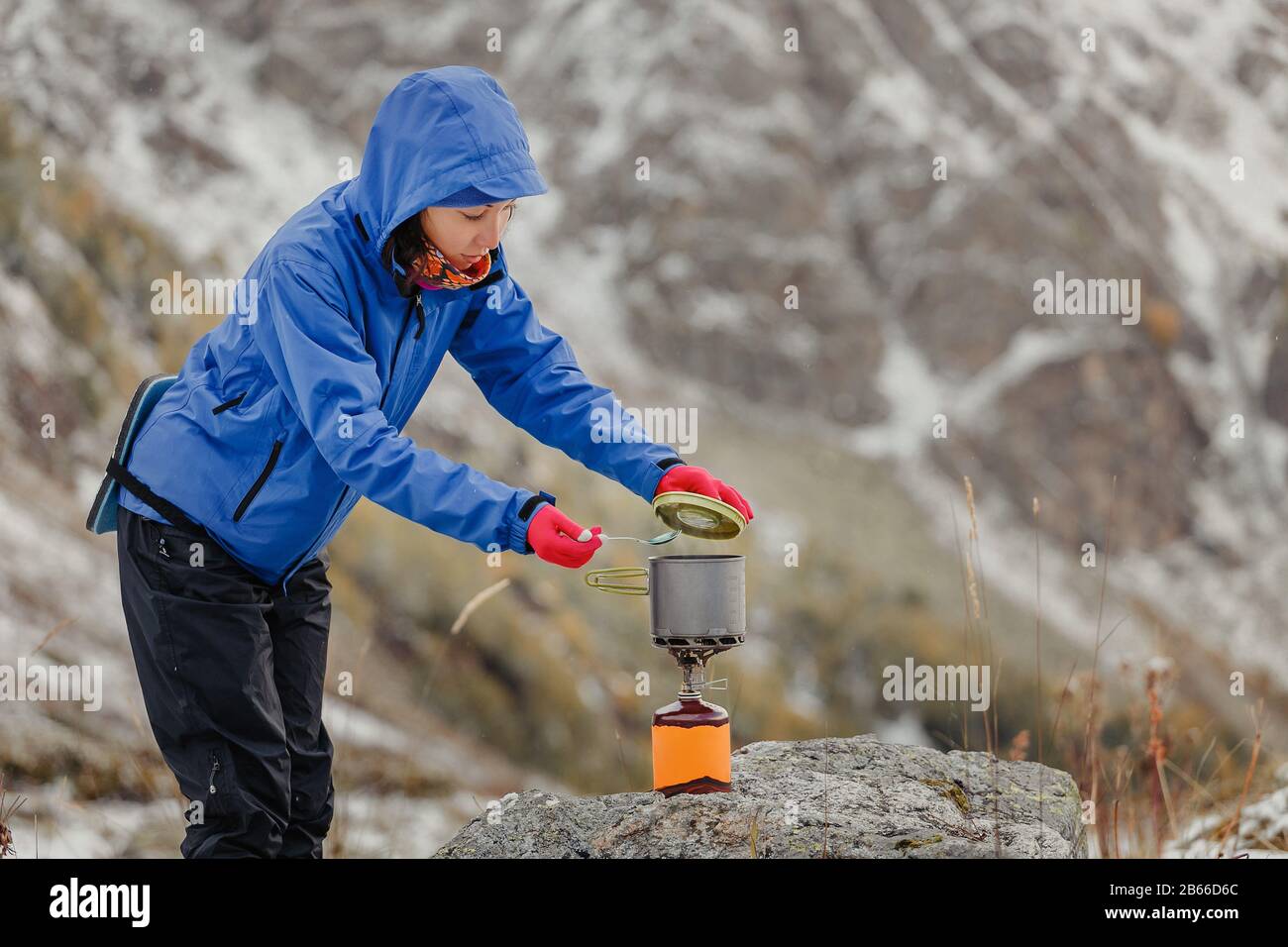 Femme bouillante sur un jet de gaz portable de camping près de la tente de randonnée dans les montagnes enneigées de la fin de l'automne Banque D'Images