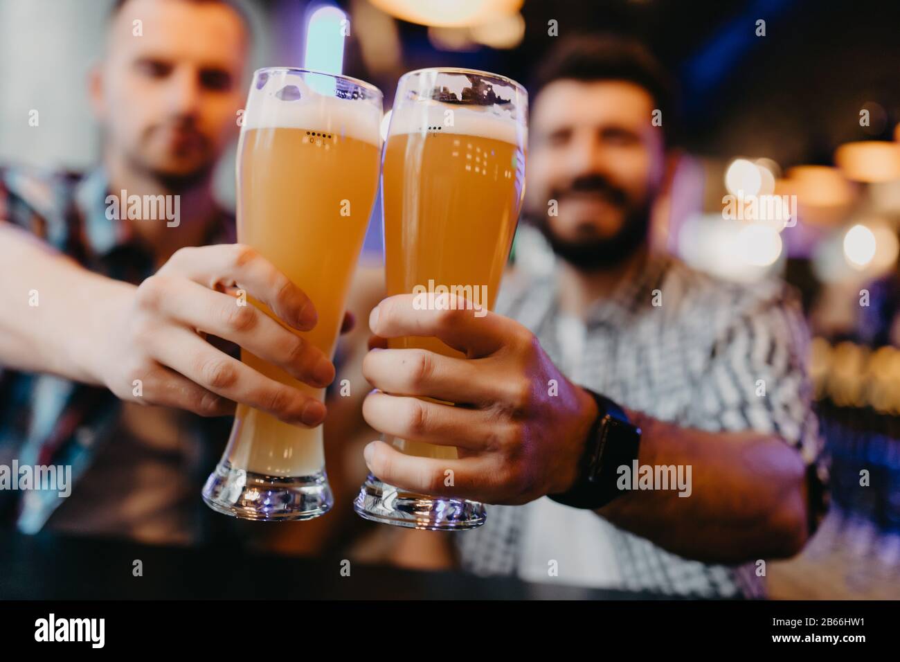 Joyeux amis qui s'inclinent avec des tasses de bière au pub, souriant. Banque D'Images