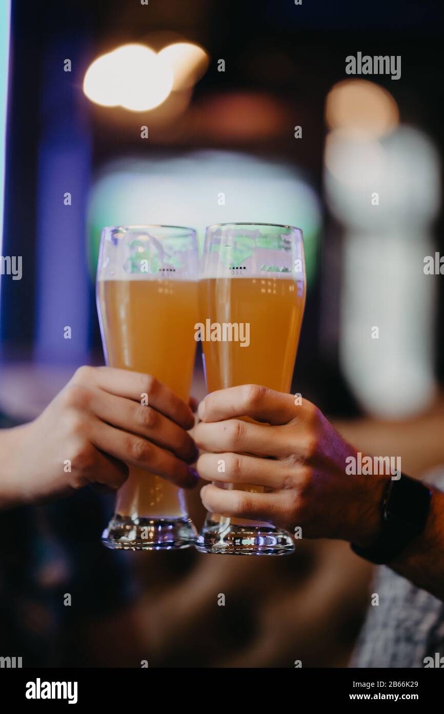 Gros plan sur les mains de deux amis en dégustant des verres de bière au pub. Banque D'Images