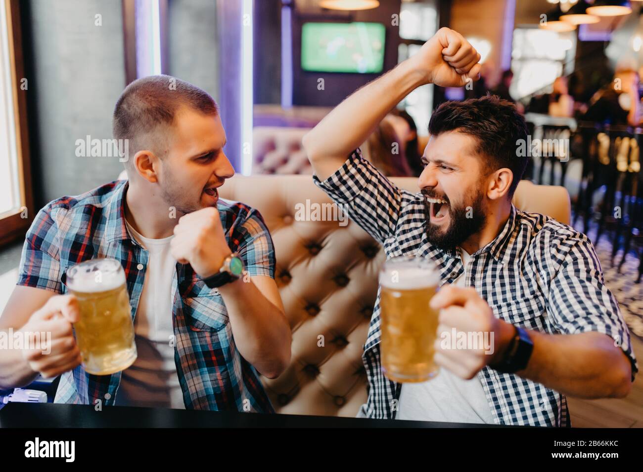 Fans deux jeunes hommes en chemise de plaid au bar ont levé les mains avec des verres de bière et criant, émotions de jeu passionnant à la télévision Banque D'Images