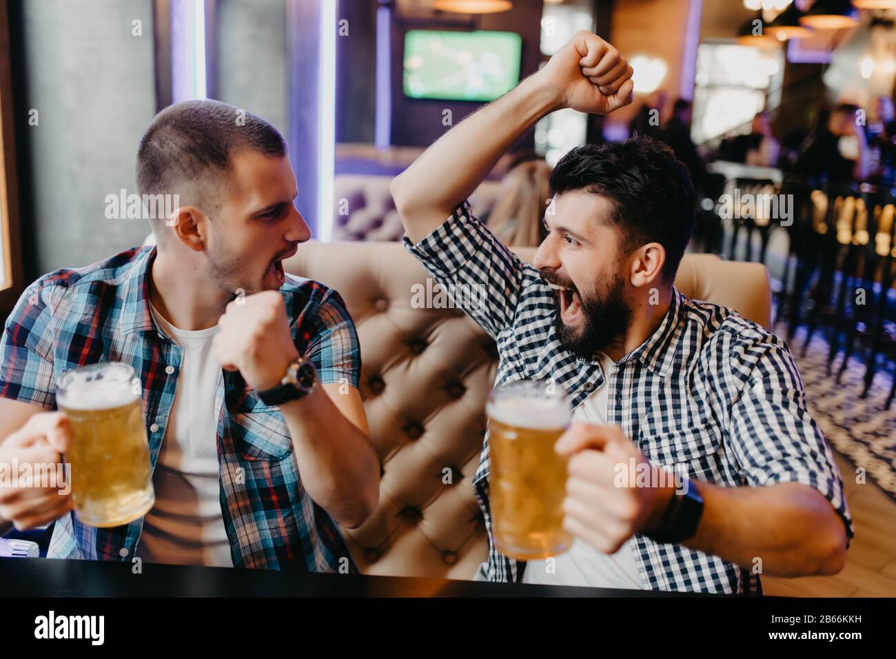 Fans deux jeunes hommes en chemise de plaid au bar ont levé les mains avec des verres de bière et criant, émotions de jeu passionnant à la télévision Banque D'Images
