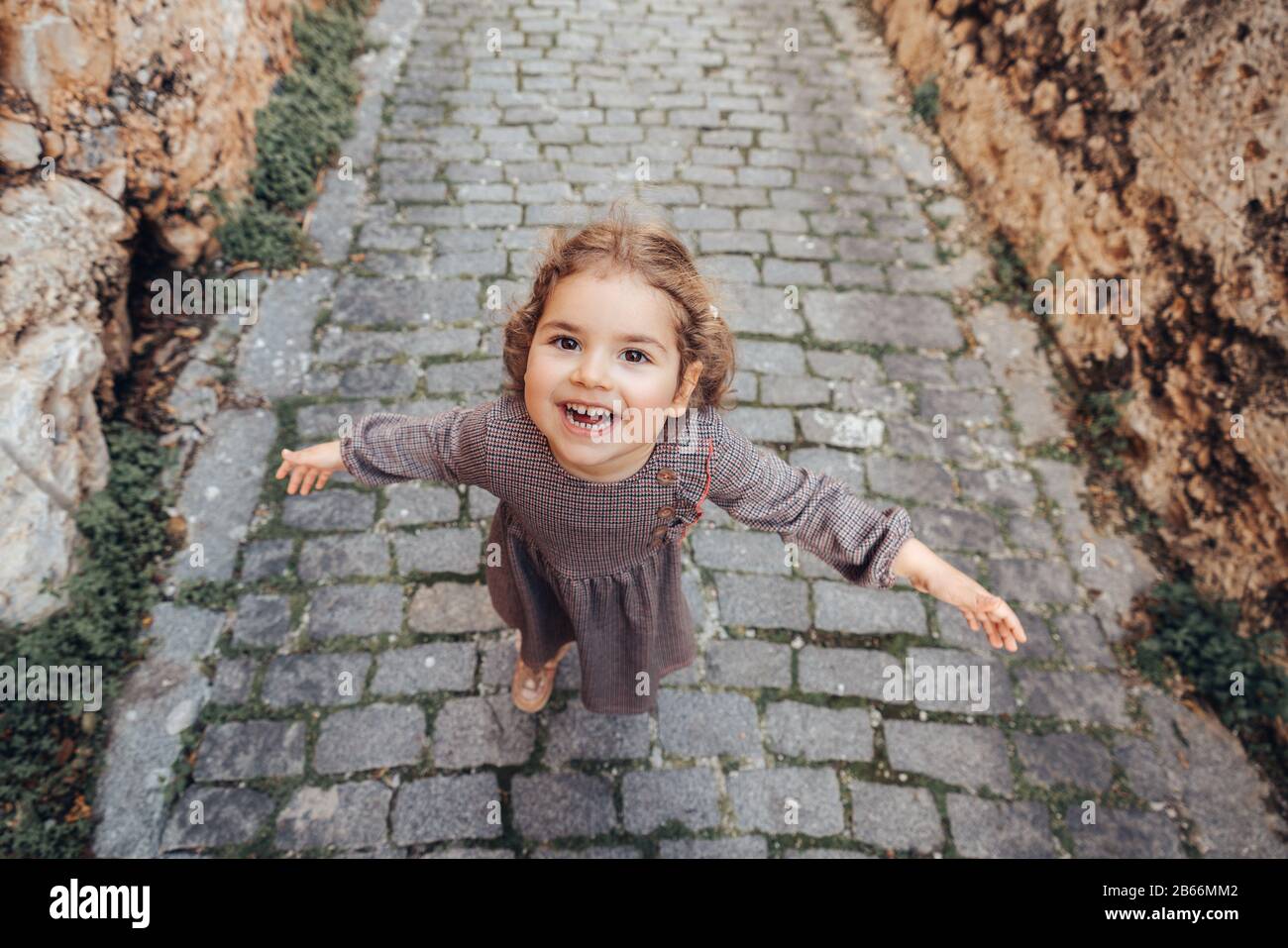 Une jolie fille de bébé tient les bras ouverts et marche sur un sentier sur une allée médiévale Banque D'Images