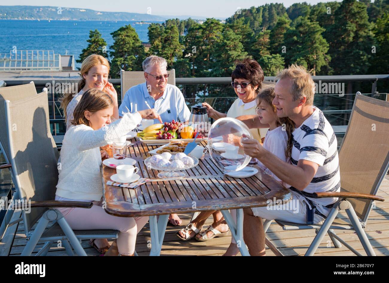 Grande famille heureuse petit déjeuner à l'extérieur sur la terrasse ensemble, assis autour de la table, boire du café. Belle vue sur la mer, chaud matin d'été. Famille Banque D'Images