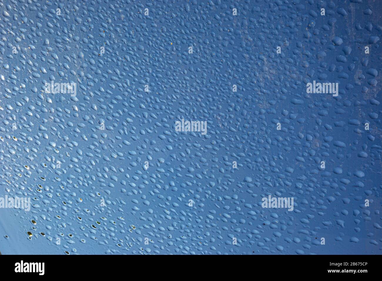 l'eau tombe sur une vitre avec des reflets et un fond bleu Banque D'Images