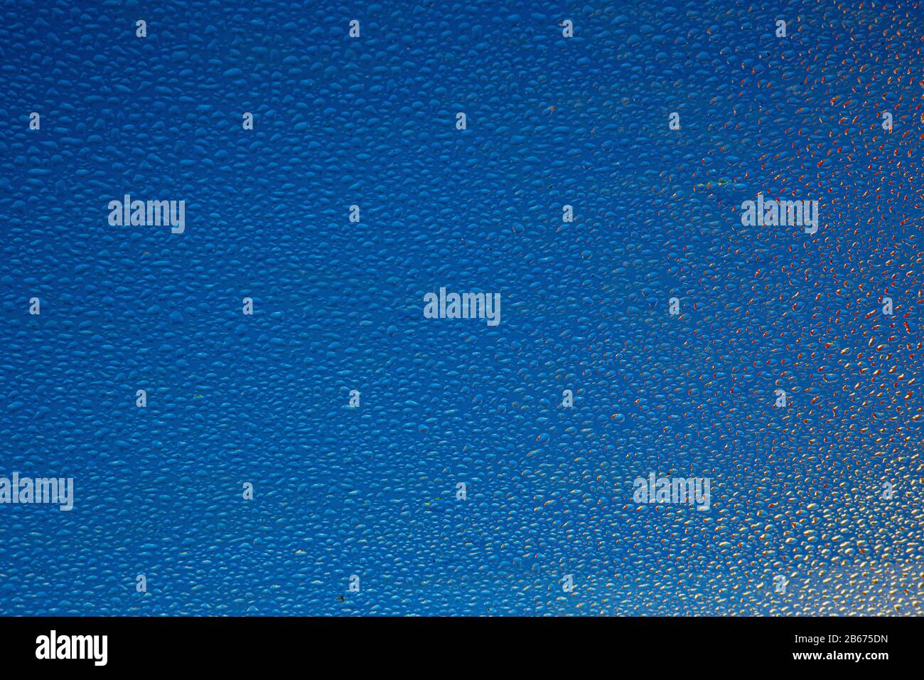 l'eau tombe sur une vitre avec des reflets et un fond bleu Banque D'Images