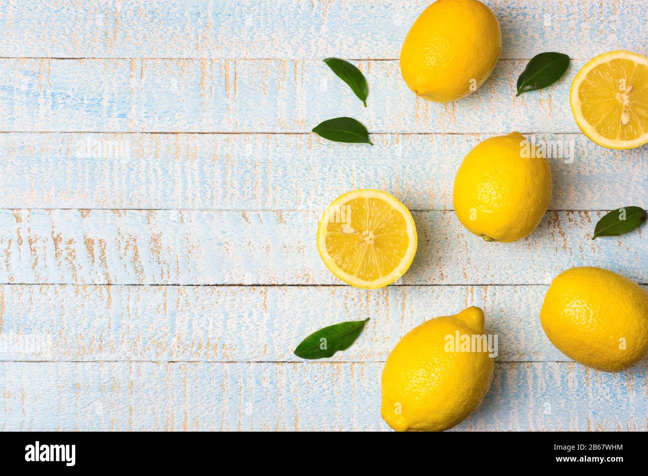 Composition plate de citrons entiers mûrs et demi-citrons avec feuilles sur fond de bois bleu clair. Espace de copie, vue de dessus. Banque D'Images