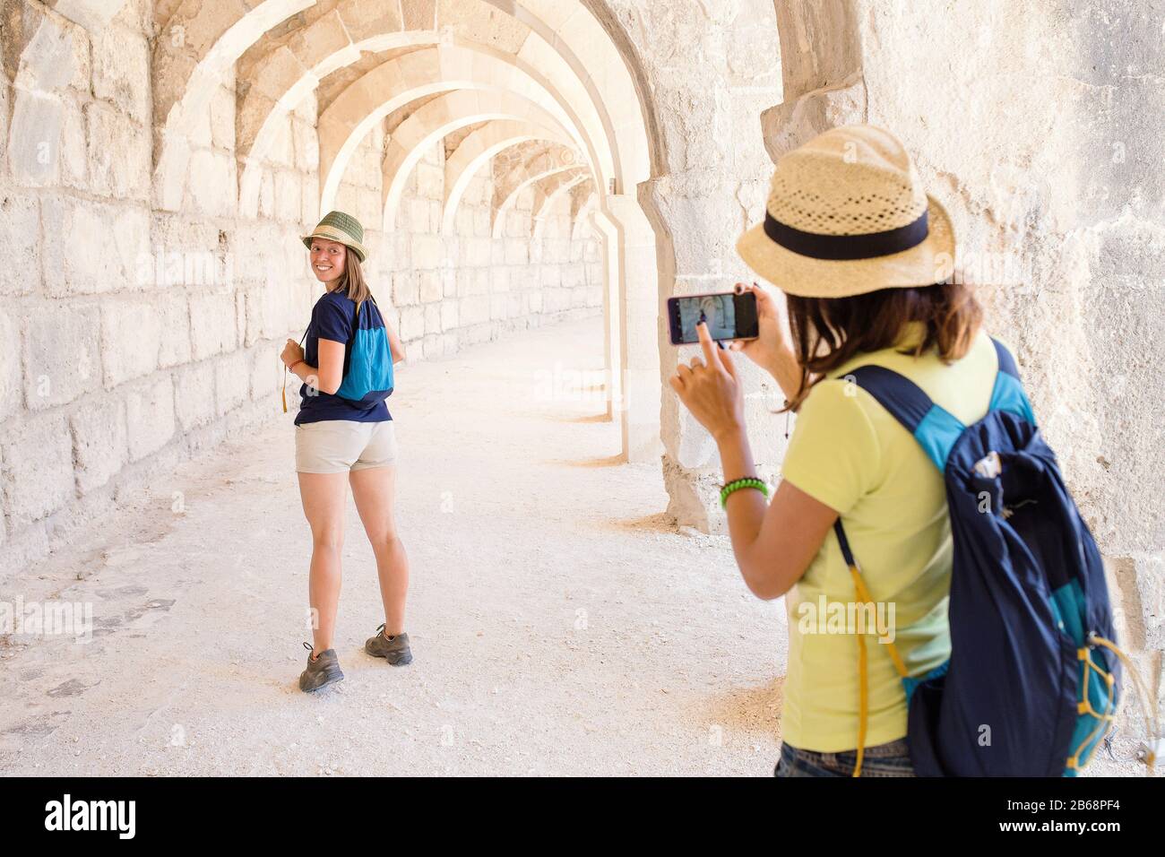 Vue arrière de la jeune femme de tourisme avec appareil photo de téléphone intelligent prenant des photos de son ami dans un bâtiment ancien Banque D'Images