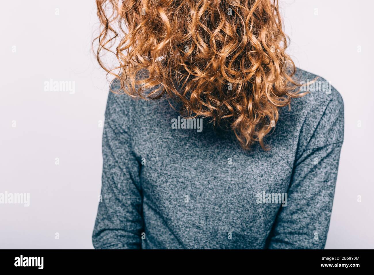 Jeune femme avec des cheveux naturellement brun vêtu d'un chemisier gris assis sur fond blanc. Banque D'Images