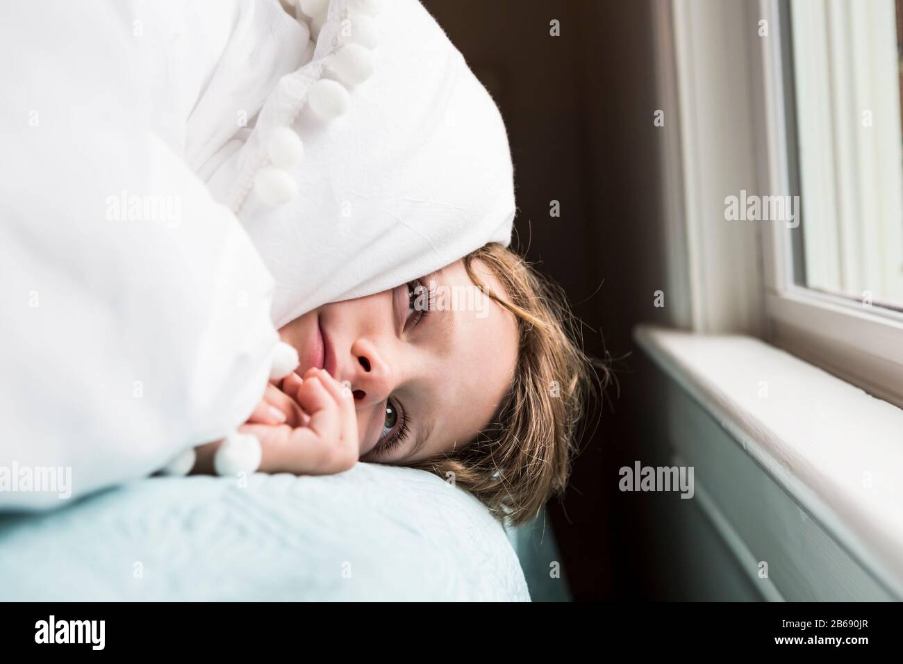 un garçon de 6 ans au lit avec des couvertures sur sa tête Banque D'Images