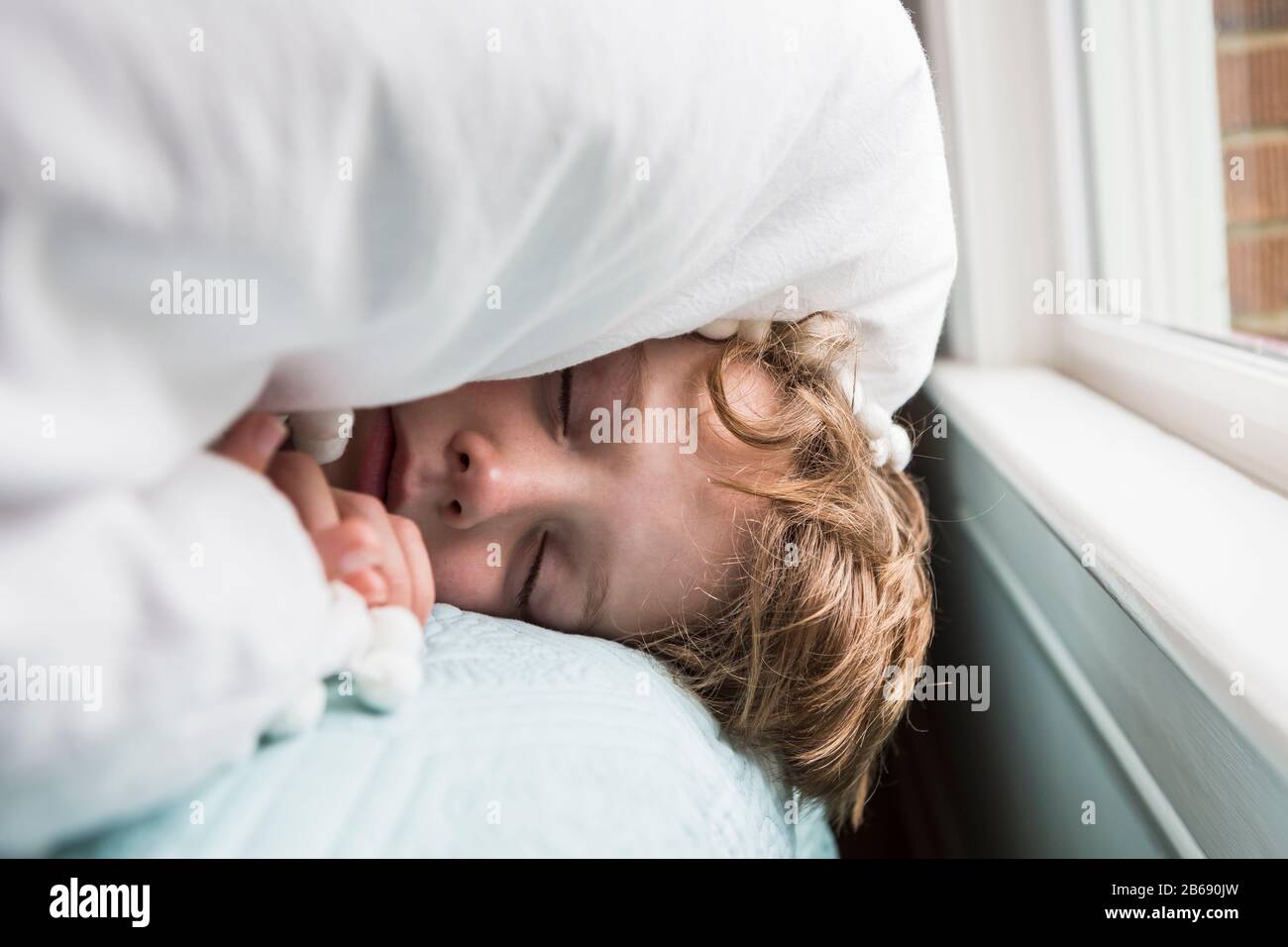 un garçon de 6 ans au lit avec des couvertures sur sa tête Banque D'Images