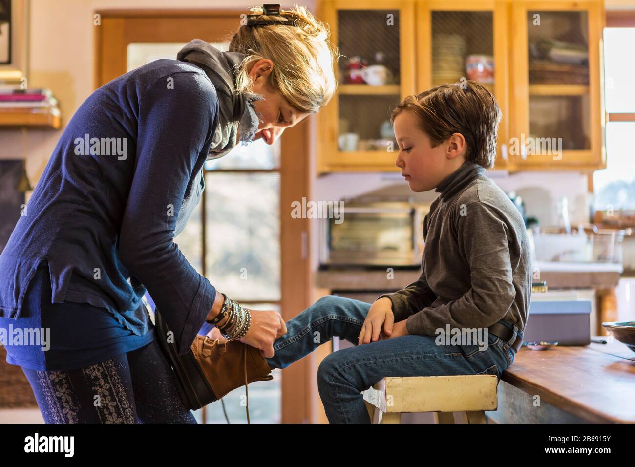 Une femme, mère mettant des bottes sur son fils de six ans en début de matinée Banque D'Images