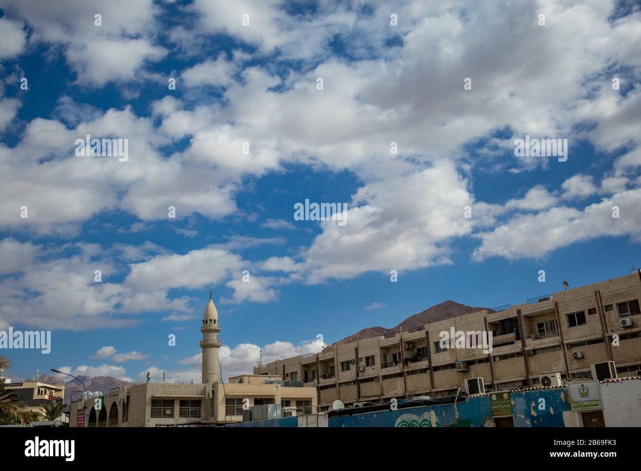 Aqaba, JORDANIE - 31 JANVIER 2020: De beaux nuages blancs d'hiver puffy se déplaçant dans le ciel au-dessus de la célèbre ville. golfe de la Mer Rouge, Royaume hachémite de Jordanie. Vue sur la rue avec mosquée et bâtiments résidentiels Banque D'Images
