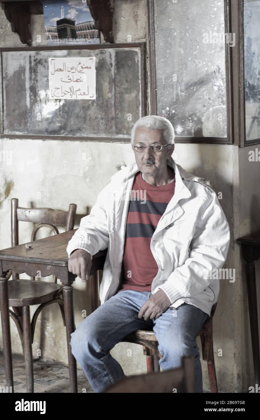 Ce portrait évocateur capture un homme âgé assis seul dans un café égyptien usé du temps. Son expression contemplative, ses cheveux blancs et sa tenue simple. Banque D'Images