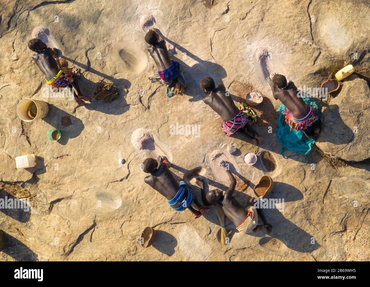 Les femmes de la tribu Larim meulant des grains de sorgho dans des trous dans un rocher, les monts Boya, Imatong, Soudan du Sud Banque D'Images