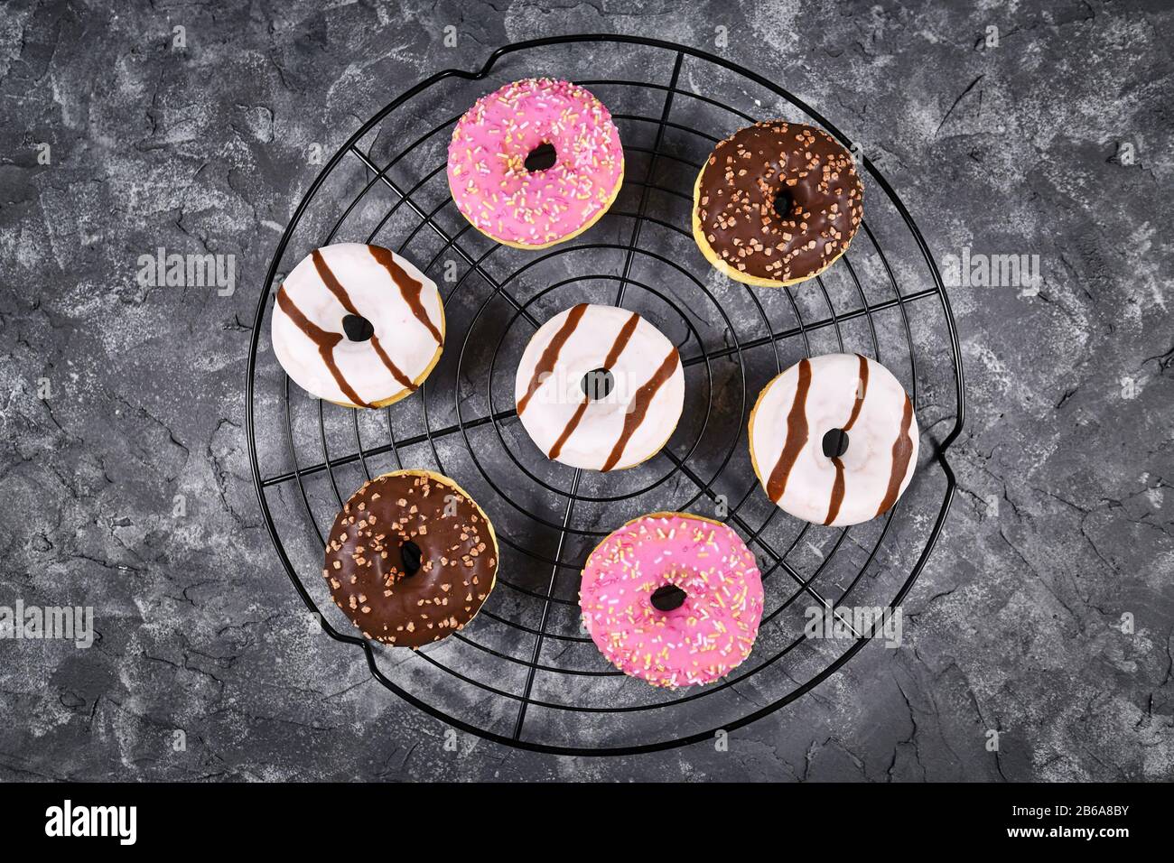 Beignets glacés avec différents chocolat blanc et brun et garniture de fraise avec des saupoules disposées en cercle sur grille de gâteau sur fond sombre de grunge Banque D'Images