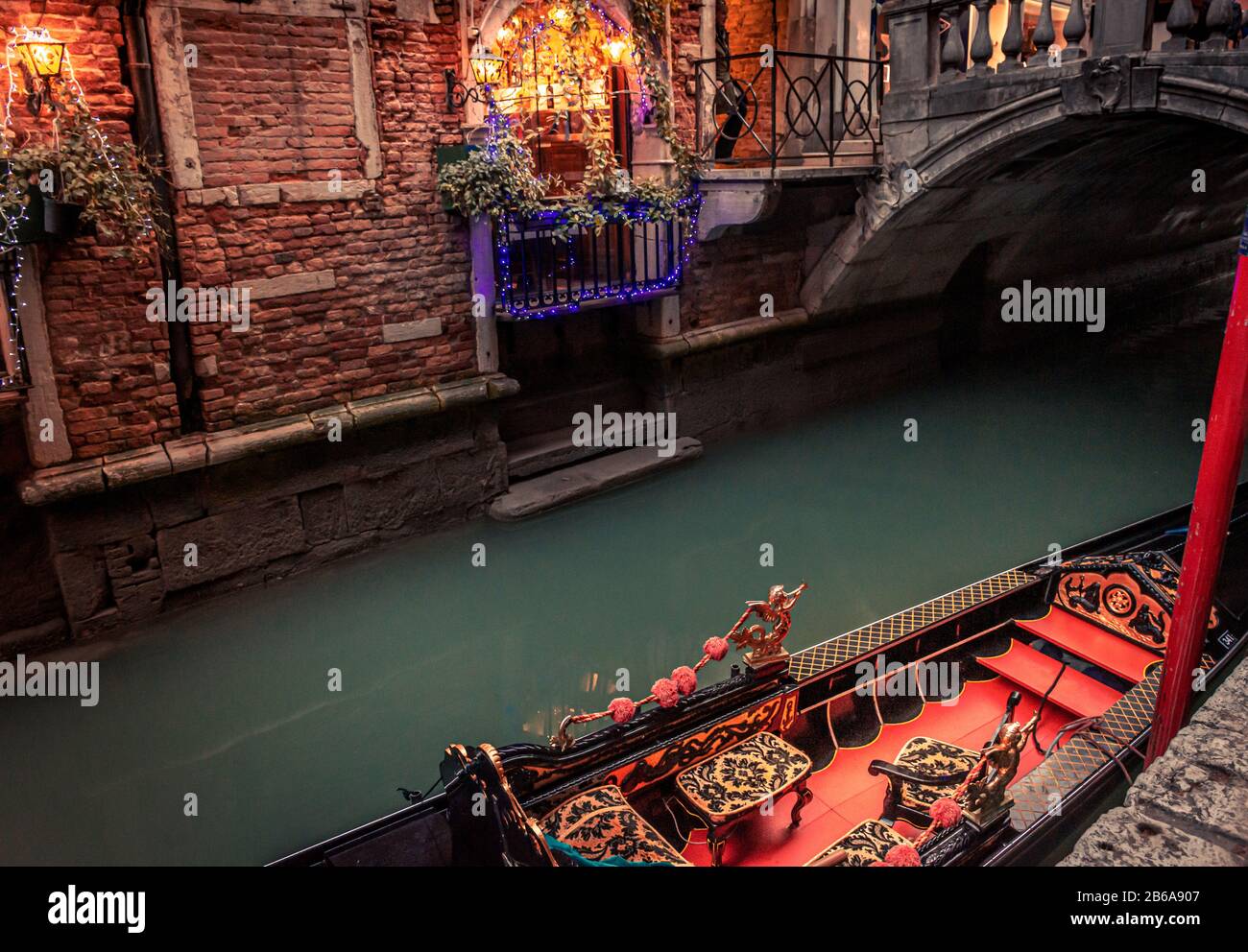 Une télécabine ornée d'un intérieur rouge et or amarré sur un canal étroit à Venise, en Italie avec un pont et des lumières de Noël en arrière-plan Banque D'Images
