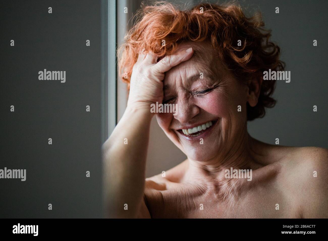 Heureuse femme mûre souriante par la fenêtre Banque D'Images