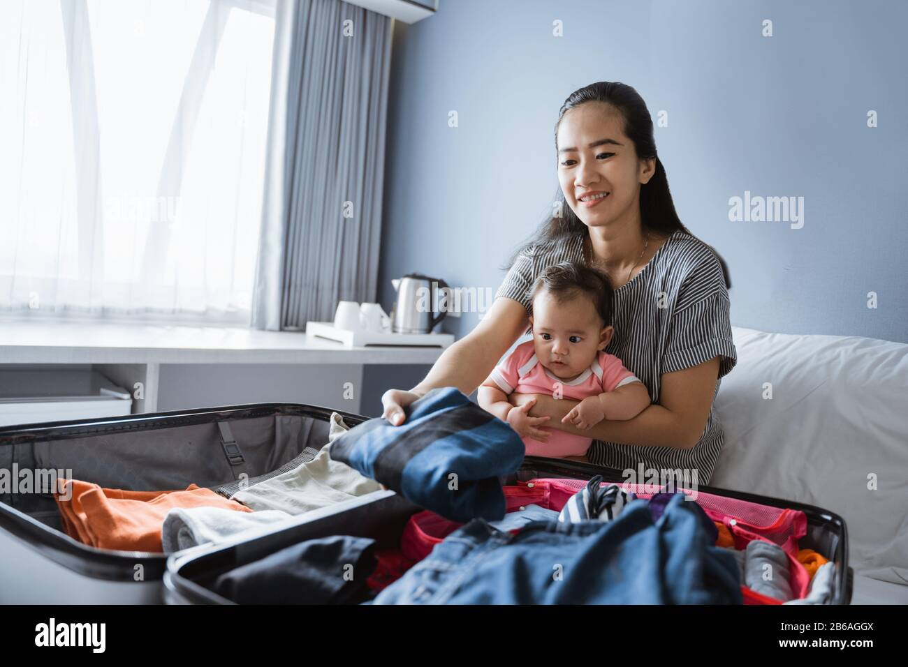 la mère asiatique est assise sur les genoux de sa fille tout en préparant des vêtements à mettre dans la valise Banque D'Images