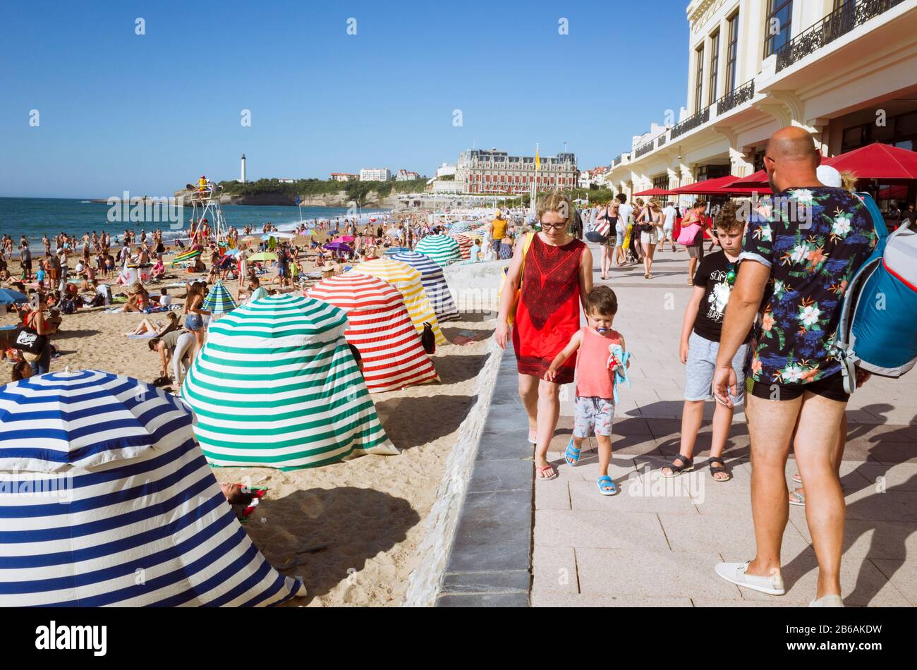 Biarritz, Pays basque français, France - 19 juillet 2019 : scène de rue avec des goéers de plage parmi des parasols colorés à la Grande Plage, le larg de la ville Banque D'Images