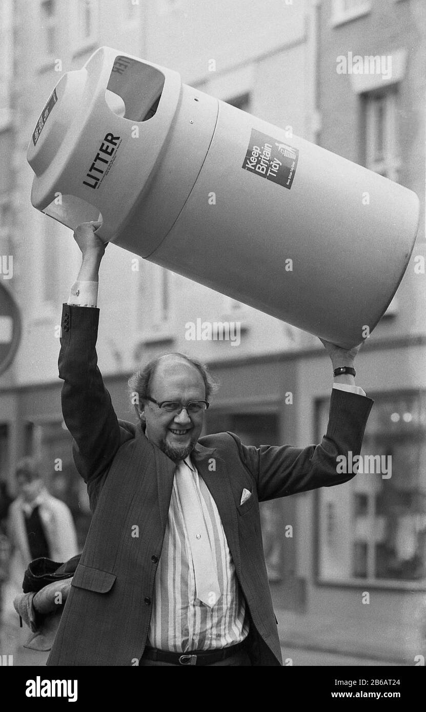 1987, historique, dans une rue haute, un homme soulevant une poubelle en plastique au-dessus de sa tête, célébrant le début de la campagne « Garder la Grande-Bretagne Bien Rangée », York, Angleterre, Royaume-Uni. Banque D'Images
