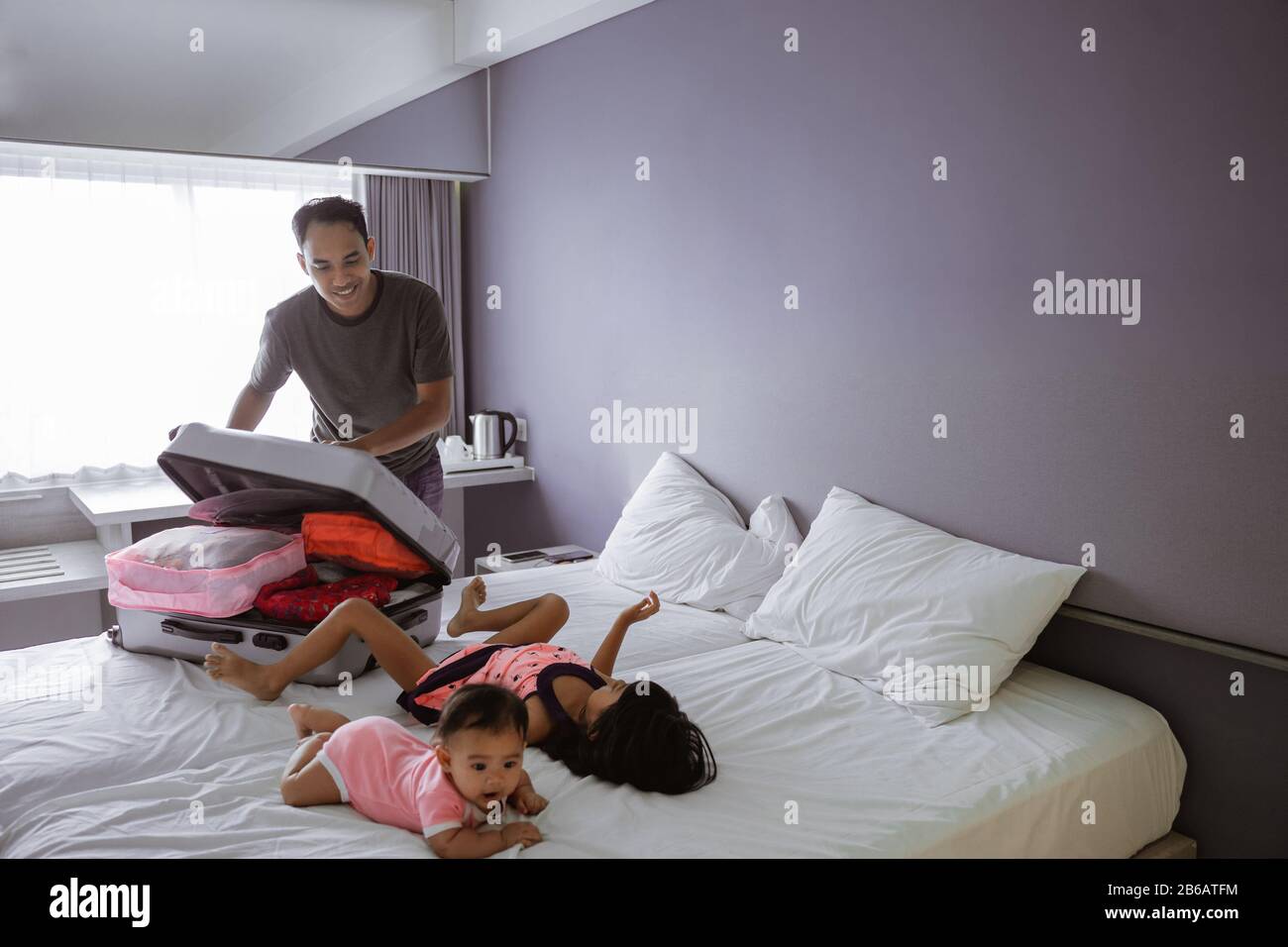 le père prépare la valise quand ses deux enfants jouent sur le lit dans la chambre Banque D'Images
