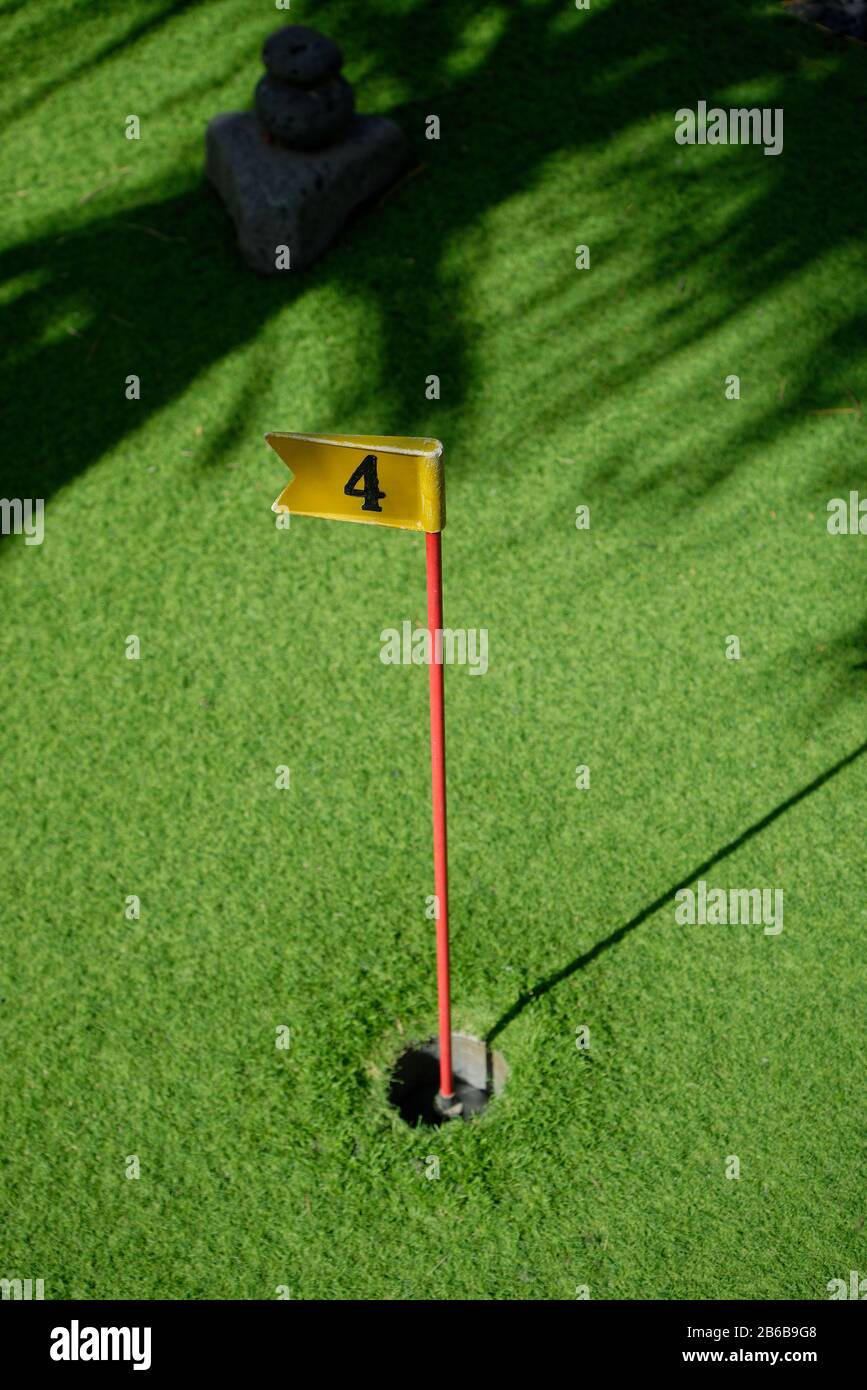 Un trou de golf à poinçonner avec un vert astrogazon et une lumière aux applis. Avec drapeau et numéro quatre sur le poteau. Banque D'Images
